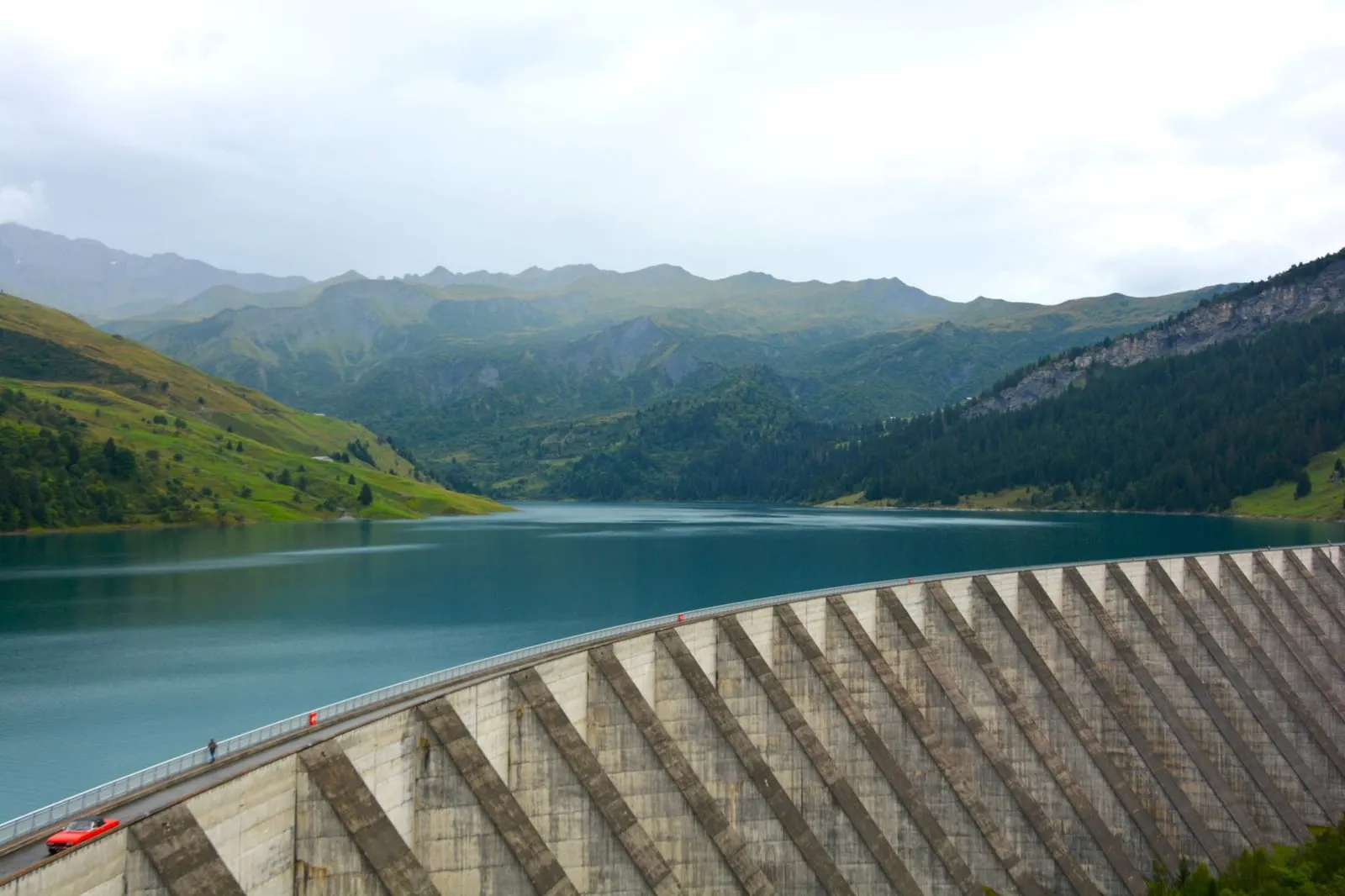 A scenic mountain landscape featuring a large dam and serene lake reflection.
