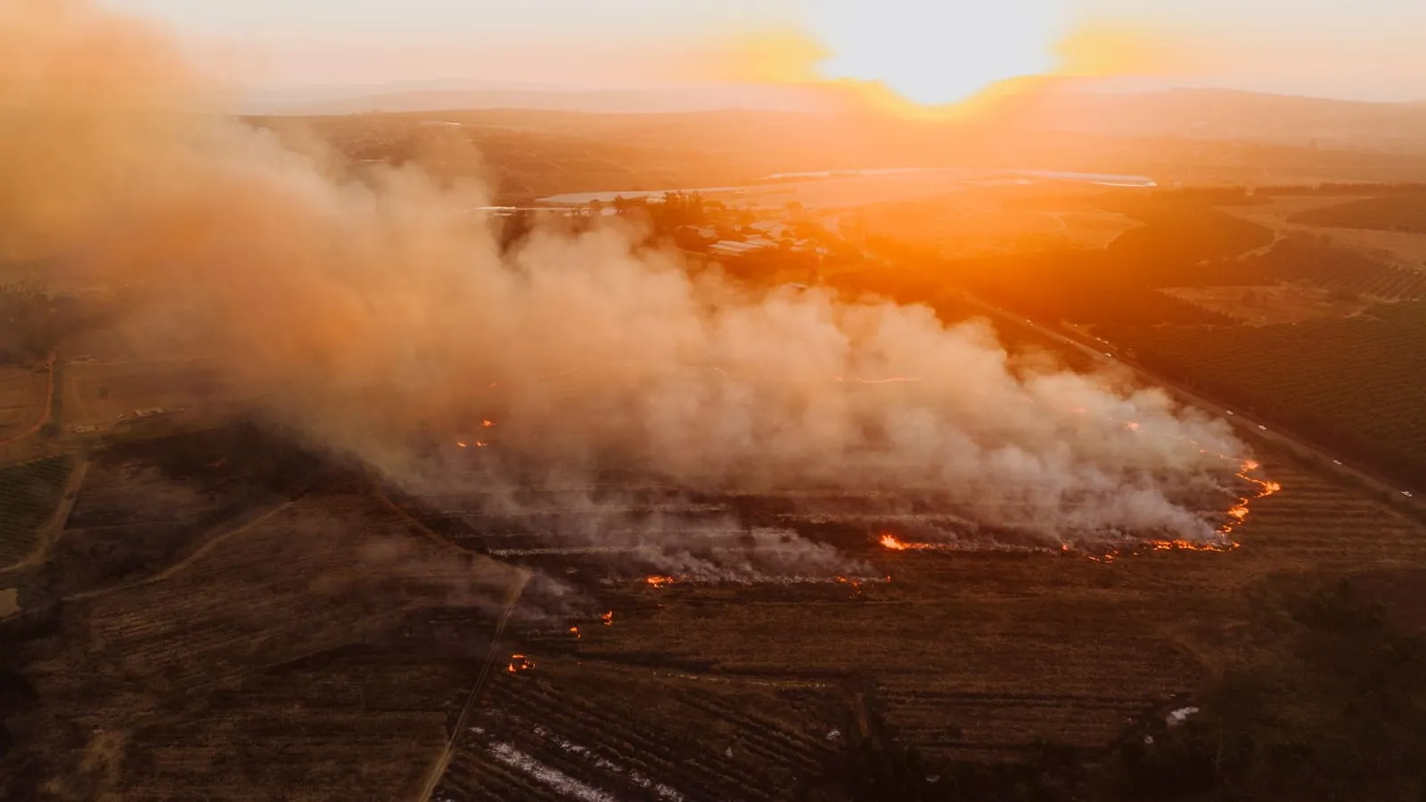 Aerial shot of a wildfire near White River, South Africa, creating dramatic sunset scenery over the landscape.