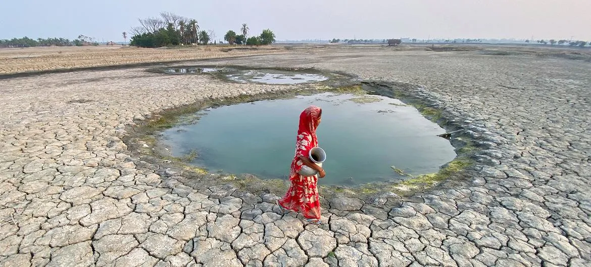 A woman in a red sari walks across a vast cracked lakebed to reach a shrinking pool of water