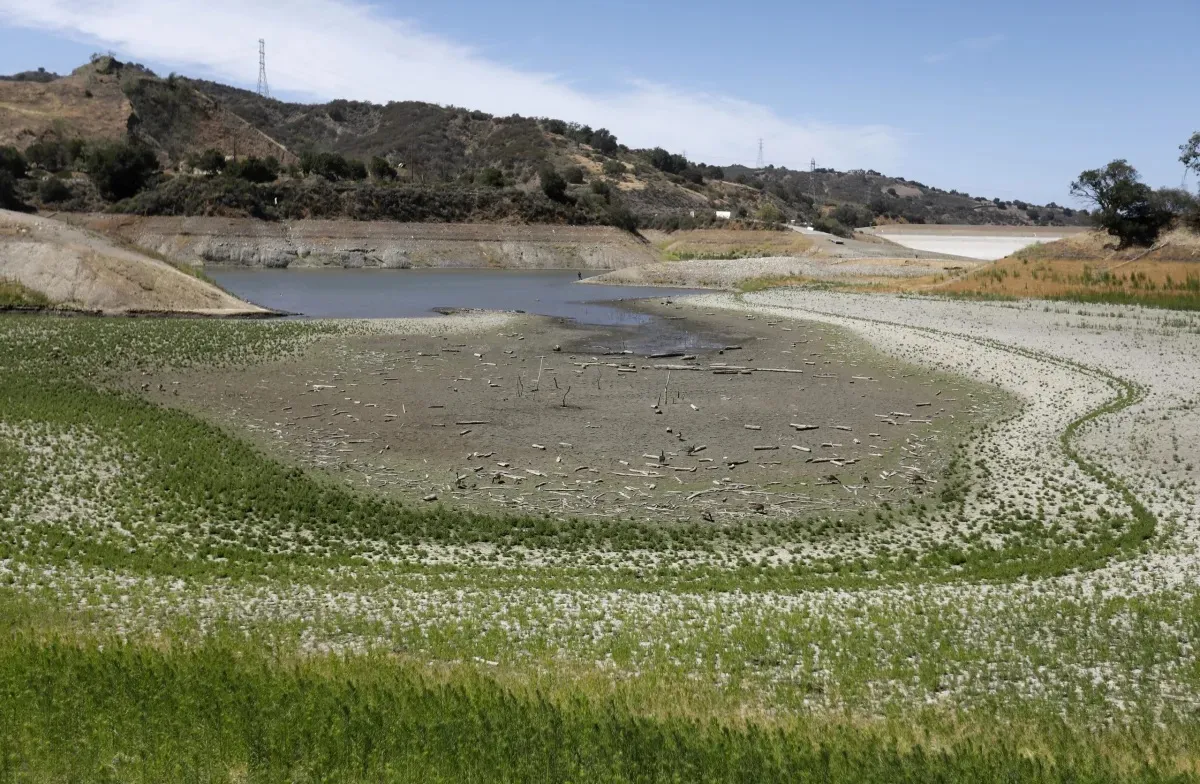 A reservoir drawn far below its high-water mark, exposing wide bands of dry, cracked shoreline