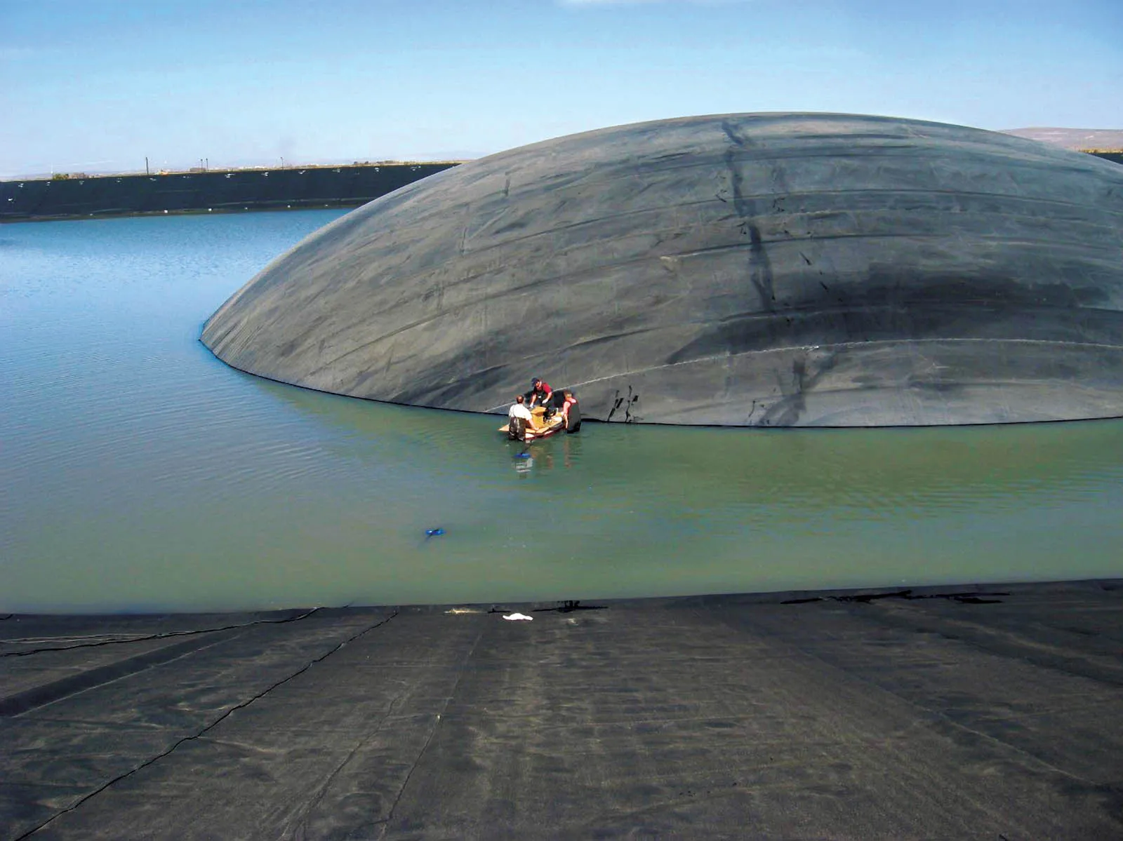 A large dome of dark geomembrane bulging up out of a pond as trapped gas lifts the continuous sheet
