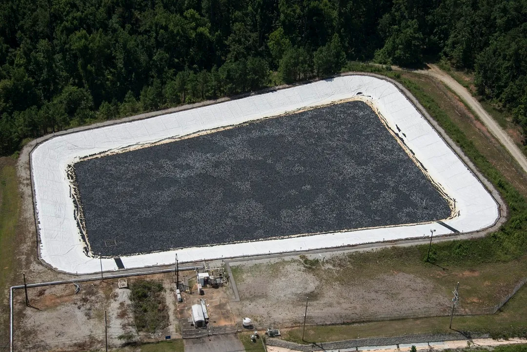 Aerial view of a rectangular basin filled with dark floating cover modules, ringed by a pale concrete apron and surrounding forest
